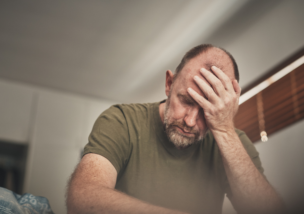 Veteran sitting on the edge of a bed holding his head during a migraine attack