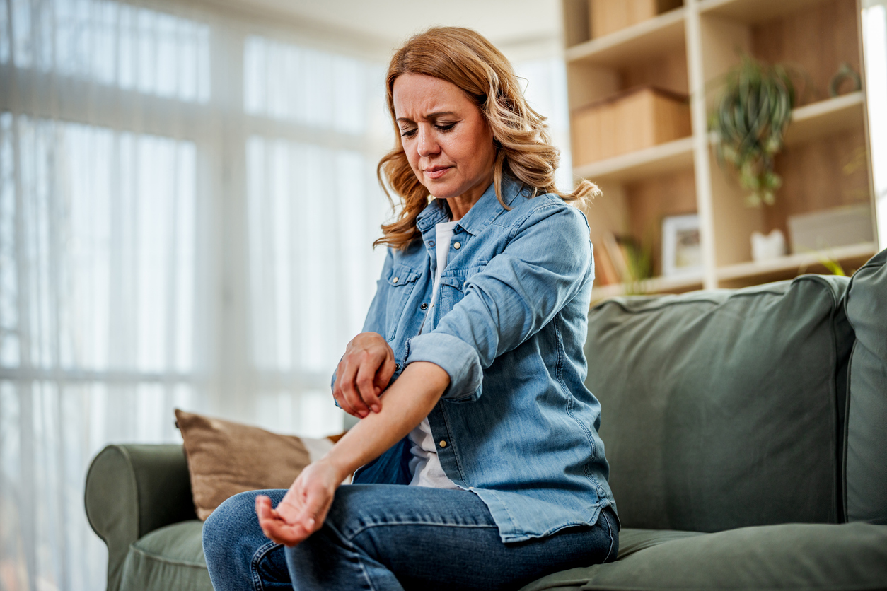 Woman seated on a couch examining an irritated patch of skin on her forearm