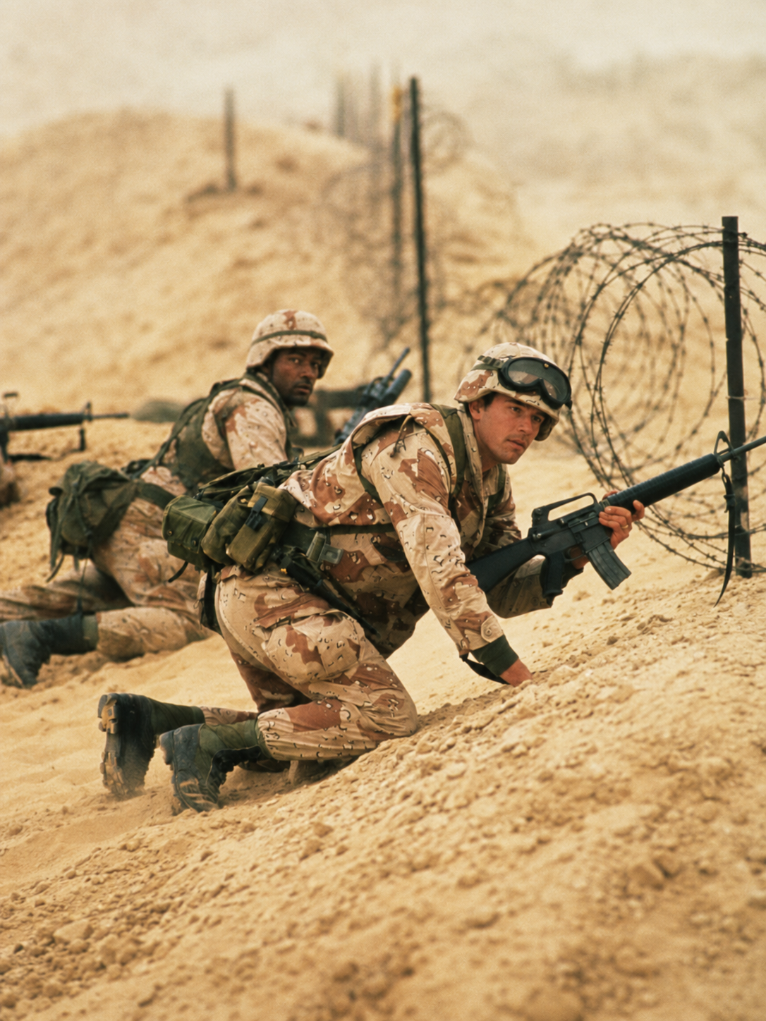 Two U.S. soldiers in desert camouflage advancing past barbed wire in the Persian Gulf