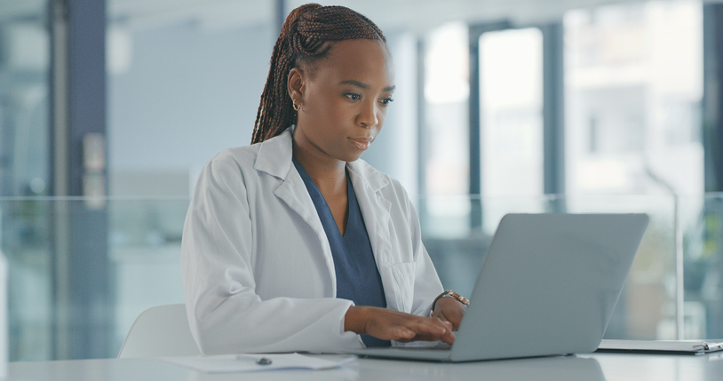 A physician in a white coat adding citations to a nexus letter on a laptop