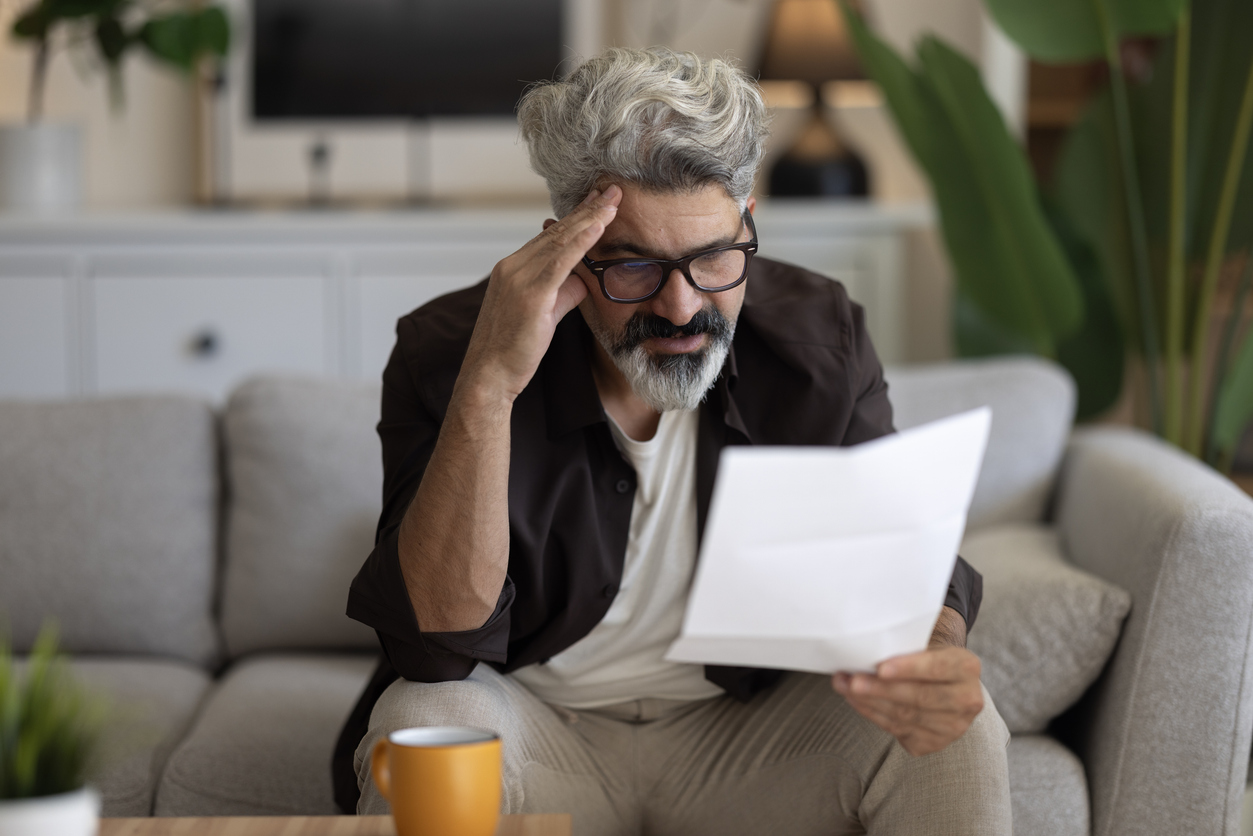A veteran sitting on his couch reading a VA denial letter with a worried expression