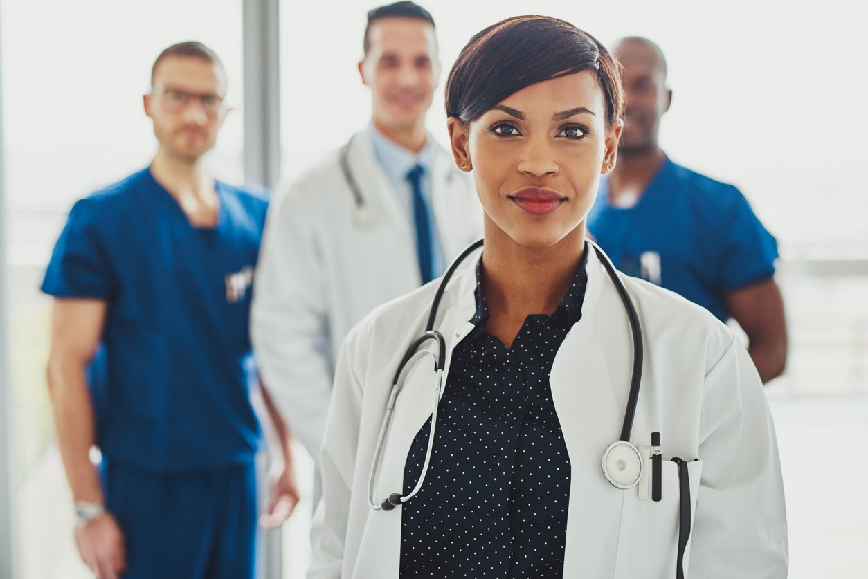 Group of physicians and clinicians in white coats and scrubs standing together