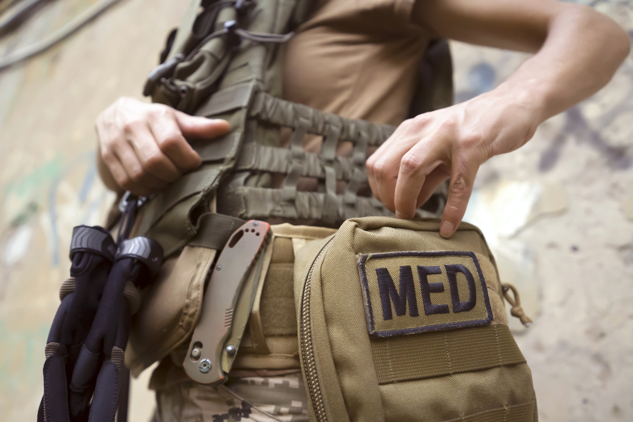 A combat medic reaching into a medical aid bag marked MED while wearing body armor