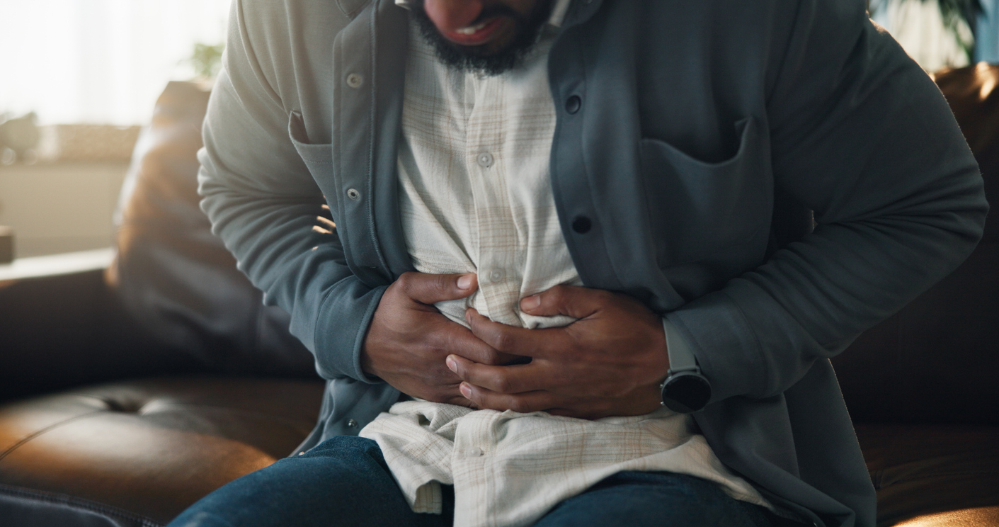 Veteran seated on a couch holding his abdomen in pain from irritable bowel syndrome