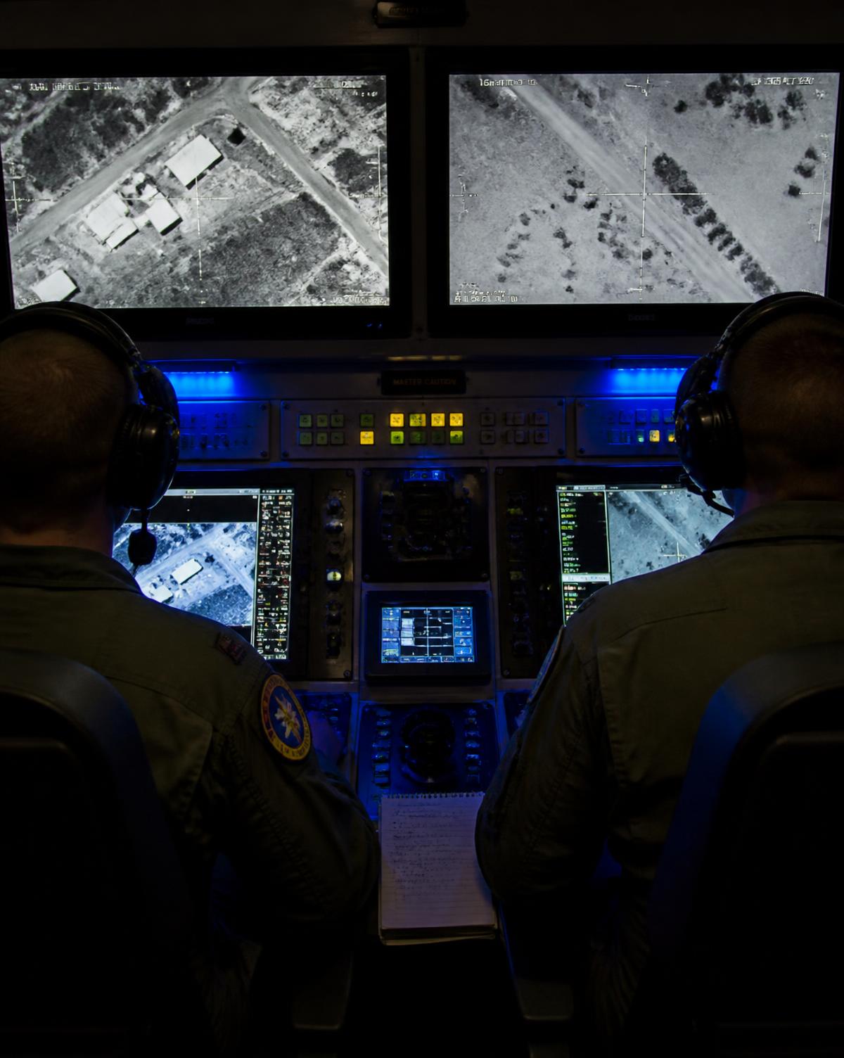 Darkened ground control station where an RPA crew watches full-motion video on multiple screens